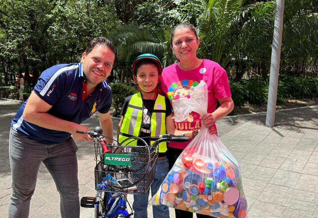 La imagen muestra a la izquierda al coordinador de fundación Tatis, David Calderón y a un niño y su mamá como benefactores entregando su donación de tapitas de plástico