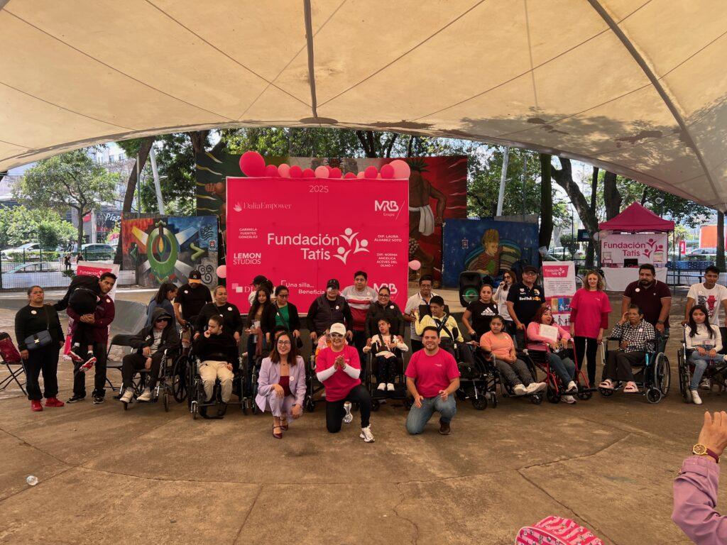 Están asistentes al evento Una Silla Beneficia Una Vida, entre ellos voluntarios de la Fundación Tatis que visten playera rosa y usuarios de sillas de ruedas beneficiarios del apoyo junto a sus familiares